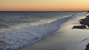 Ein Strand mit sanft anschwellenden Wellen, einem klaren Himmel und einer fernen Küstenlinie.