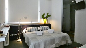 Et soveværelse med en seng, et natbord, en lampe, en kaktus og et fjernsyn ophængt på væggen.