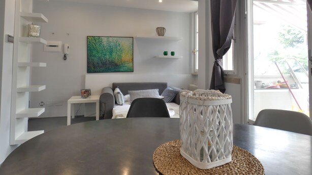 En moderne stue med spisebord, sofa og et stort vindue med gardiner.