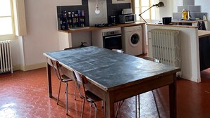 A kitchen with a table and chairs, a washing machine, a radiator, and a window. - Gîte au Château Jonquier 2 (Séguret)