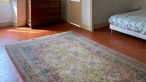 A bedroom with a wooden dresser, a painting, a door, and a bed with a floral bedspread. - Gîte au Château Jonquier 2 (Séguret)