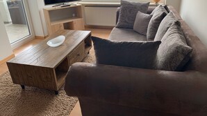 Una sala de estar con un sofá marrón, una mesa de centro de madera y un televisor de pantalla plana sobre un soporte de madera.