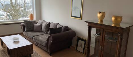 A living room with a brown sofa, a wooden coffee table, a glass cabinet with decorative items, and a framed picture on the wall.