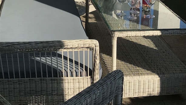 Un patio al aire libre con muebles de mimbre, una mesa de vidrio y detalles decorativos.