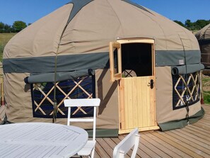 A large, dome-shaped yurt with a wooden door and windows, a white table, and a white chair outside.