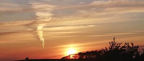 A sunset over a flat landscape with a clear sky and a visible contrail.
