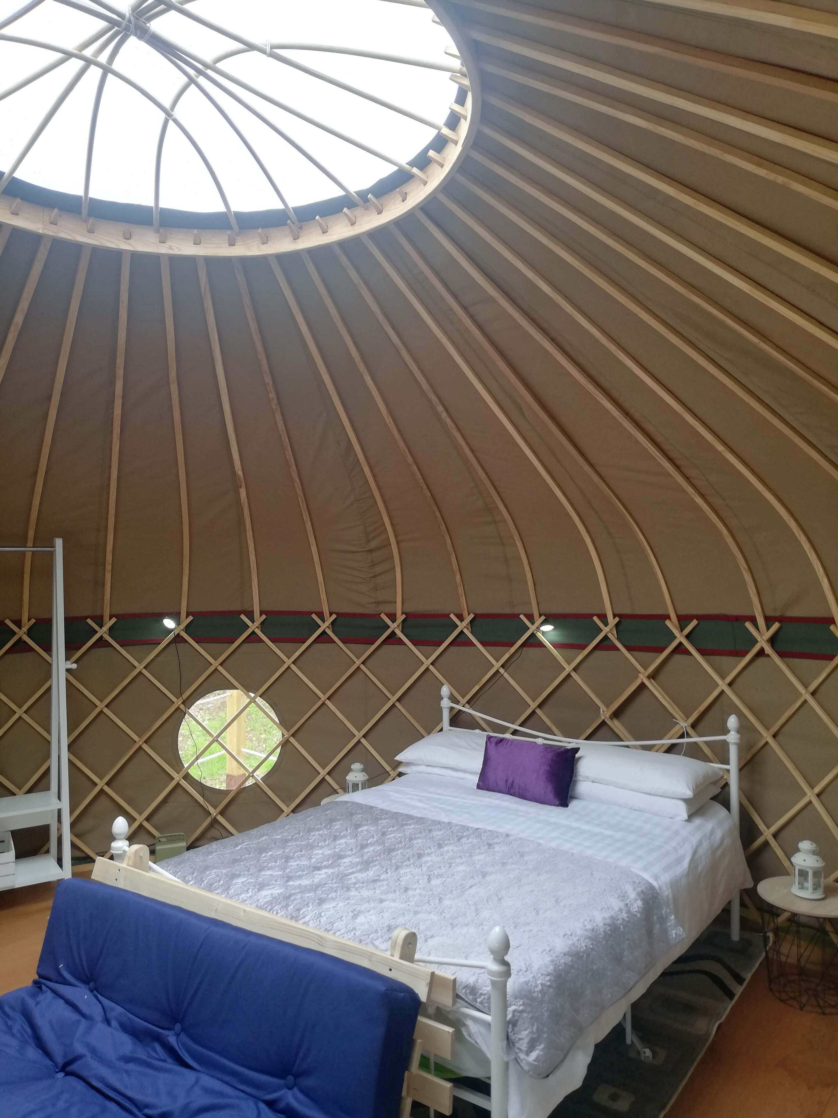 A yurt interior with a bed, a blue sofa, and a small table with a lantern.