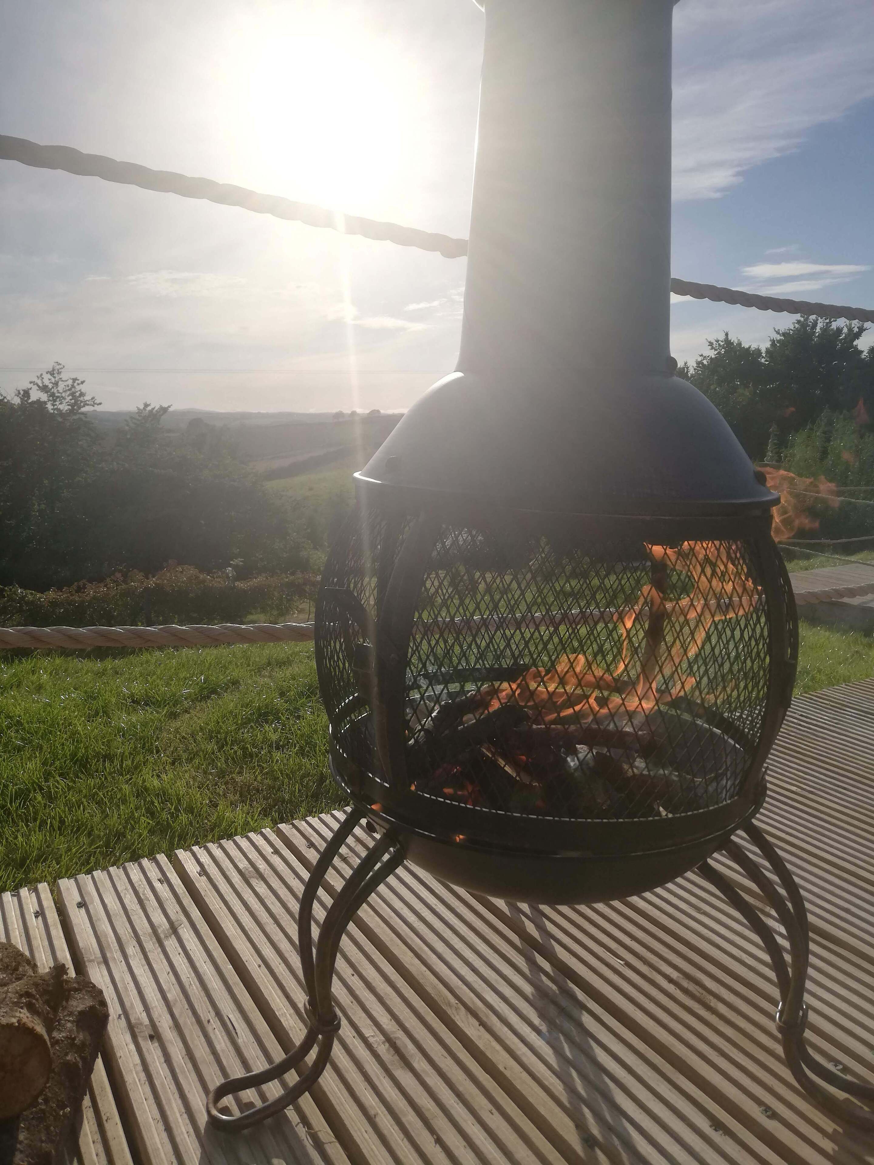 Una parrilla de metal con un cerramiento de malla, ubicada en una terraza de madera con un área verde de fondo.