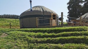 A geodesic dome structure with a chimney, surrounded by a grassy field and a gravel path. - Looe Yurts (Looe)
