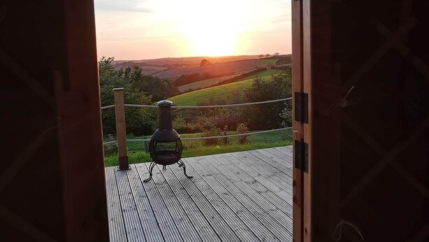 A wooden deck with a barbecue grill, overlooking a rural landscape during sunset. - Looe Yurts (Looe)