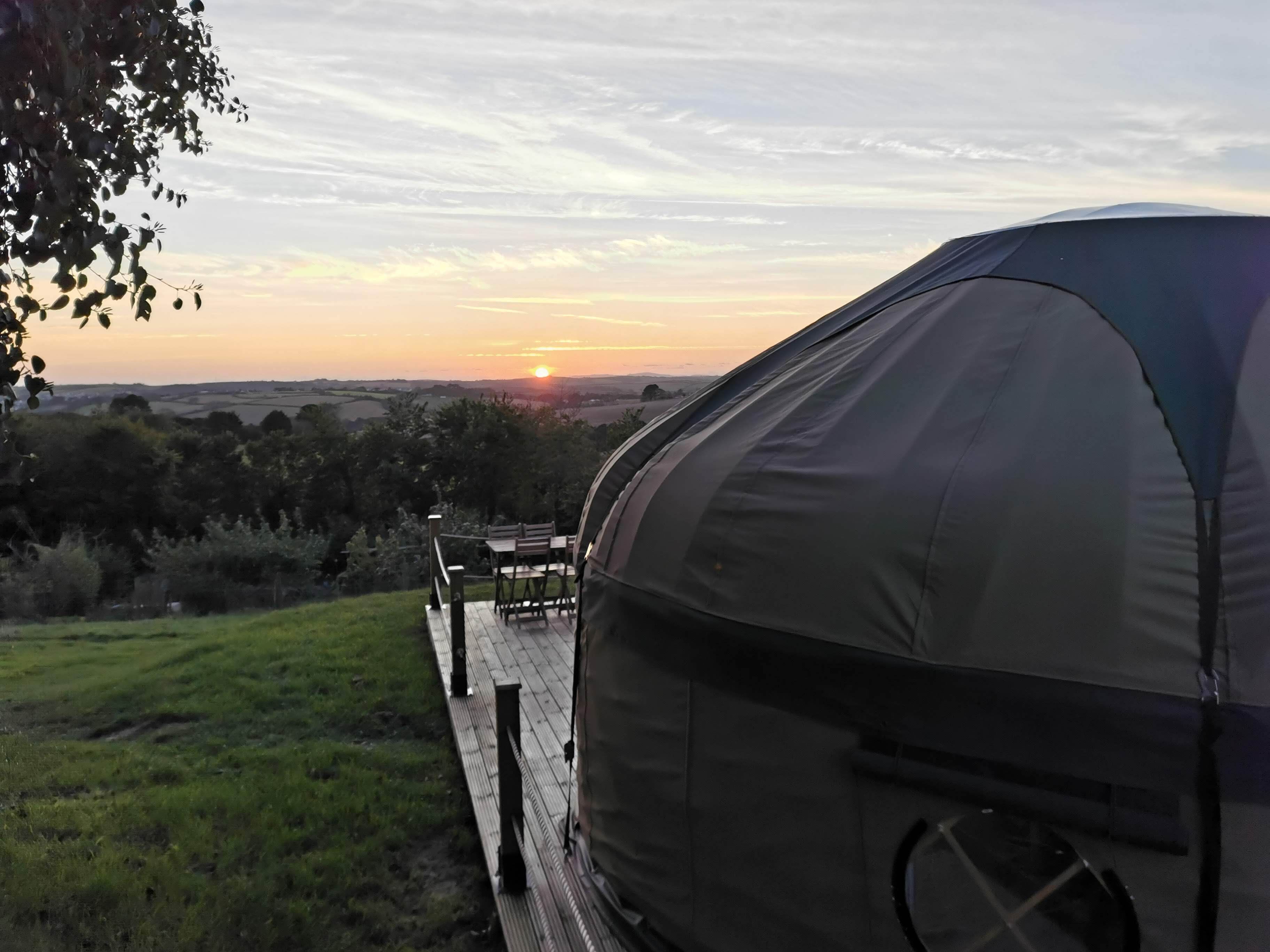 A tent with a view of the sunset over a grassy landscape and a wooden deck with chairs.
