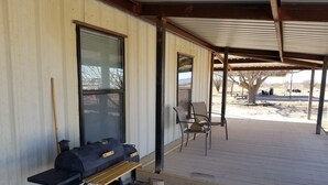 Un patio exterior con una parrilla, una mesa de madera y dos sillas.