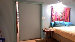 Un dormitorio con cama, mesita de noche, ventana con cortinas y puerta.