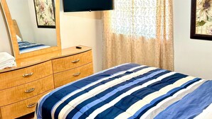Une chambre à coucher avec un lit, une commode, un téléviseur et une fenêtre avec des rideaux.