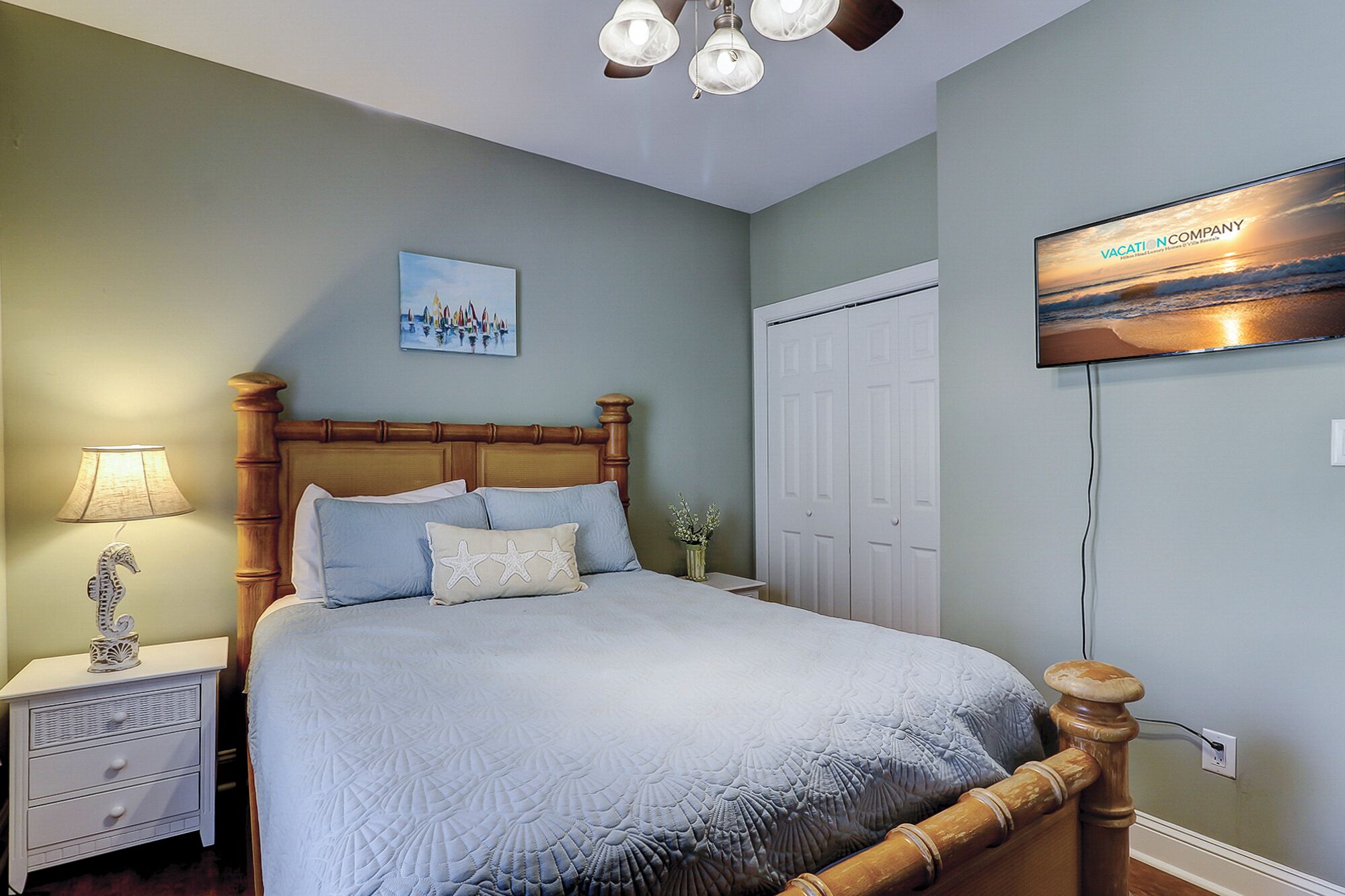 A bedroom with a bed, nightstands, a lamp, a painting, a wardrobe, and a TV mounted on the wall.