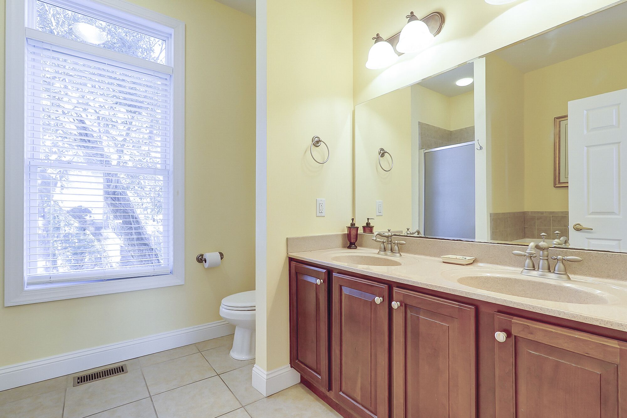 A bathroom with a toilet, a sink with a mirror, and a window with blinds.
