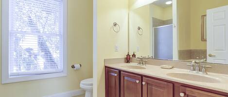 A bathroom with a toilet, a sink with a mirror, and a window with blinds.