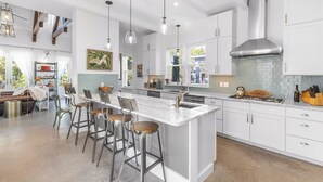 Una cocina moderna con armarios blancos, una isla grande con taburetes de bar, iluminación colgante y una campana extractora de acero inoxidable.