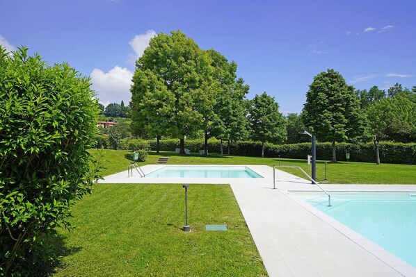 A rectangular swimming pool with a white deck, surrounded by well-maintained grass and trees.