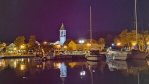 A nighttime marina with boats docked, a church with a bell tower, and illuminated buildings.