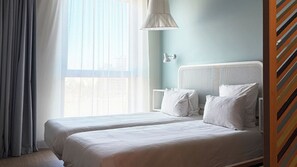Habitación de hotel con dos camas, una ventana con cortinas, una lámpara blanca y una pared azul claro.