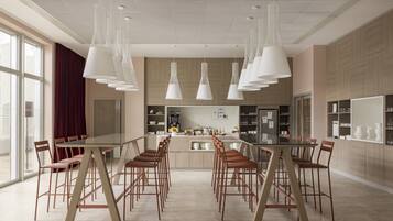 A modern kitchen with a long dining table and chairs, pendant lights, and a view of the city through large windows.