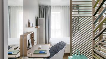 Une chambre d’hôtel moderne équipée d’un lit, d’un bureau avec une chaise, d’une télévision et d’une fenêtre avec des rideaux.