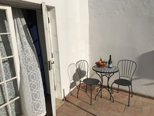 Eine offene Tür, die auf eine Terrasse mit einem für zwei Personen gedecktem Tisch, einer Obstschale und einer Weinflasche führt.