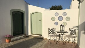 Ein Innenhof mit gefliestem Boden, einer grünen Tür, einem kleinen Tisch mit Stühlen und dekorativen Tellern an der Wand.