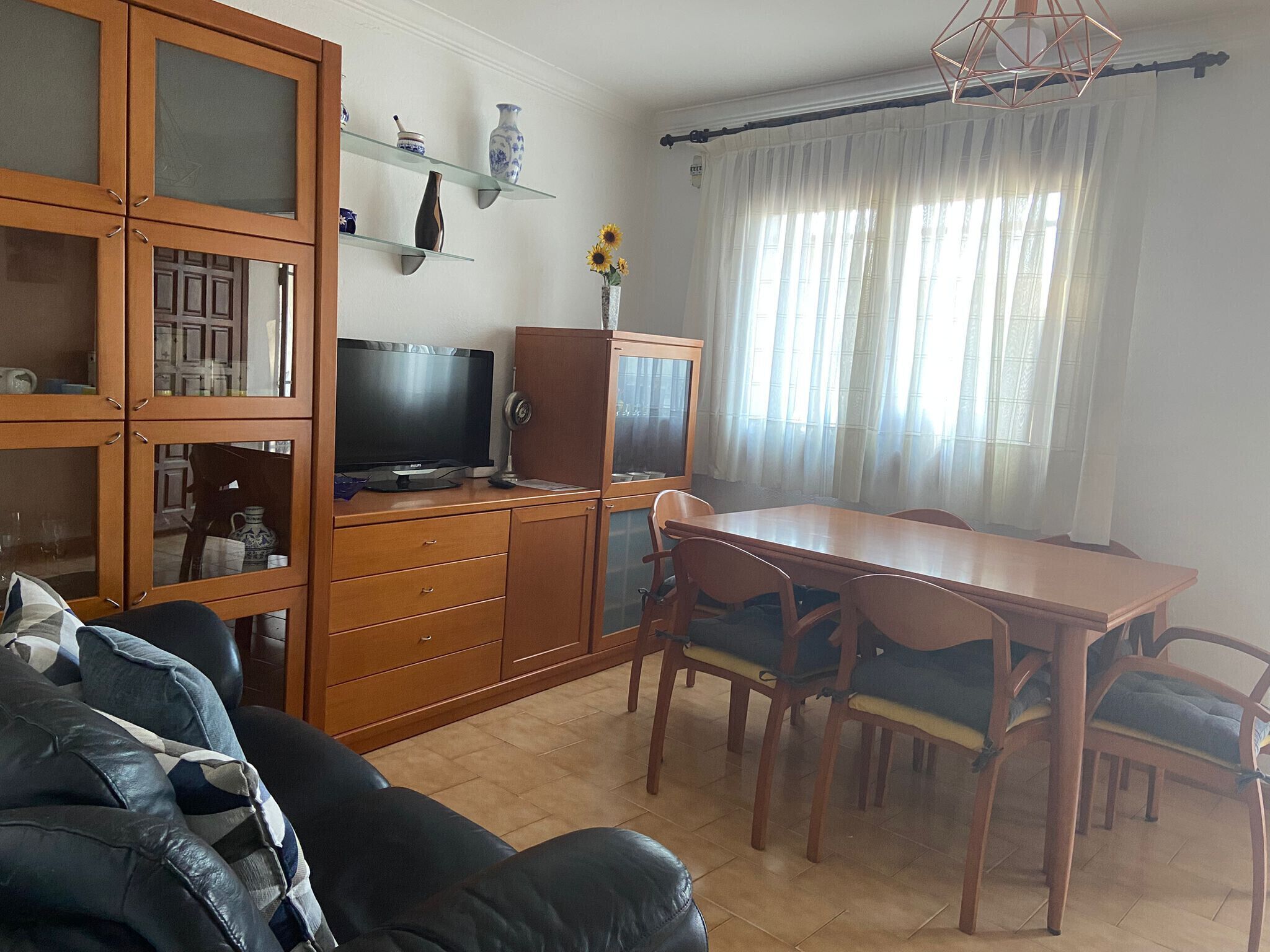 A living room with a TV, wooden cabinets, a dining table with chairs, and a window with curtains.