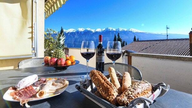 Ein Tisch mit verschiedenen Speisen, zwei Gläsern Rotwein und einer Weinflasche, vor einer Kulisse schneebedeckter Berge.