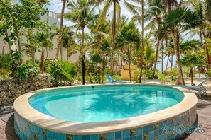 Uma piscina circular com borda azulejada, cercada por palmeiras e vista para o oceano.