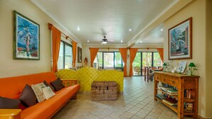 A spacious living room with a yellow sofa, orange couch, and a wooden side table with books.