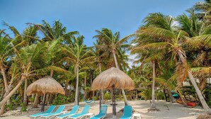 A beach with thatched umbrellas, lounge chairs, and palm trees.