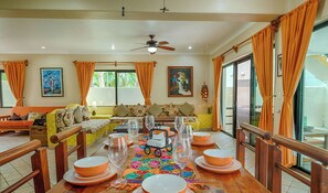 Uma área de refeições com mesa de madeira posta para uma refeição, cercada por sofás e cadeiras.