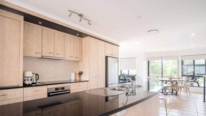 A modern kitchen with light wood cabinets, a black countertop, stainless steel appliances, and a dining area with a view.