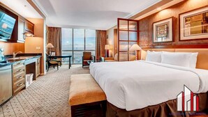 Habitación de hotel con una cama grande, un escritorio con silla, una mesita con una silla, una ventana con vistas y un televisor en la pared.