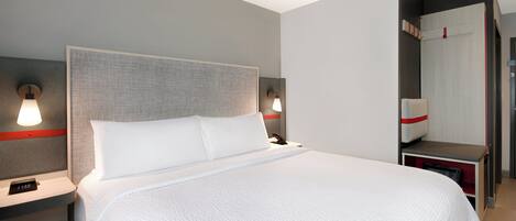 Ein modernes Hotelzimmer mit einem großen Bett, zwei Nachttischen mit Lampen, einem Beistelltisch und einem Kleiderschrank.