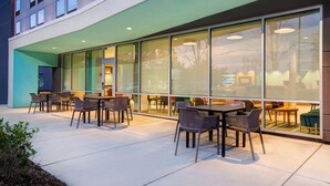 An outdoor seating area with tables and chairs, large windows, and a modern building facade. - avid Hotel Fort Mill - Carowinds Blvd by IHG (Fort Mill)