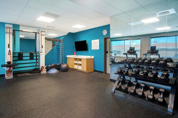 Une salle de sport équipée de matériel d’exercice, d’un téléviseur fixé au mur et d’une fenêtre donnant sur un beau paysage.