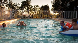 Ein Schwimmbecken mit einem umzäunten Bereich, umgeben von Bäumen und einem Holzbau.