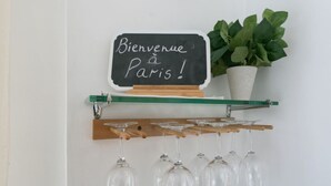 A blackboard with "Bienvenue à Paris!" written on it, a green shelf with wine glasses, and a potted plant. - Beautiful flat in Montparnasse (Paris)