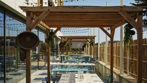 Un espace de restauration en plein air doté de plusieurs tables et chaises, d’une structure en forme de pergola et de guirlandes lumineuses.