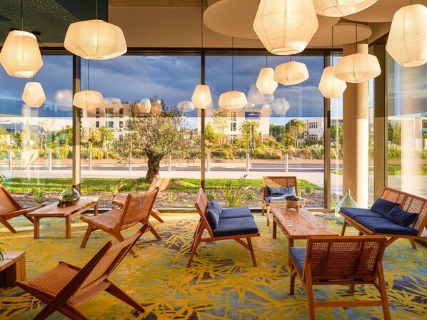 A modern lounge area with wicker furniture, large windows, and hanging paper lanterns.