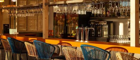 A bar area with wicker chairs, hanging light fixtures, and a bar counter with glasses and bottles.