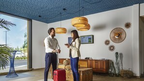 Un hall d'hôtel moderne avec une grande fenêtre, des lampes suspendues en osier au plafond et un comptoir d'accueil.