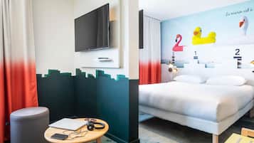 A hotel room with a bed, a TV, a desk with a laptop, headphones, and a mobile phone.