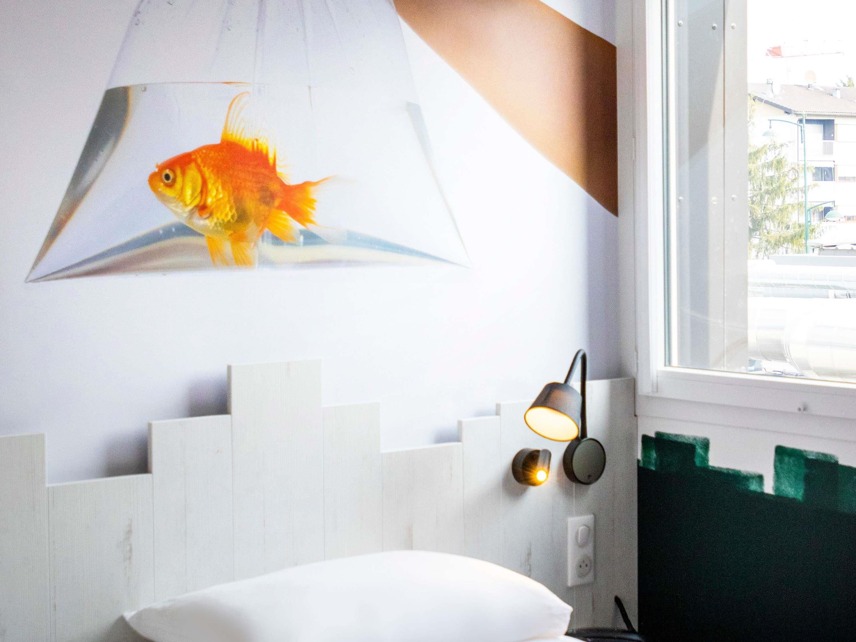 Una habitación con una cama blanca, una lámpara de pared y una ilustración de un pez.