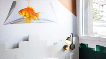 Una habitación con una cama blanca, una lámpara de pared y una ilustración de un pez.