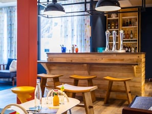 Uma área de bar com banquetas de madeira, balcão e garrafas.